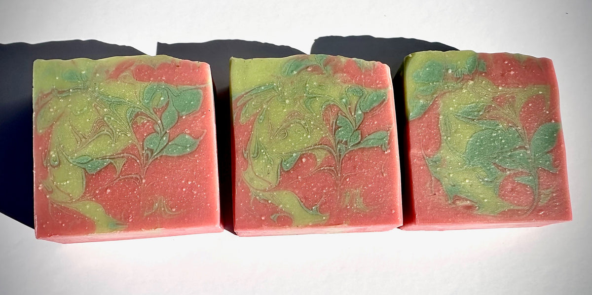 Three bars of soap with green and pink marbled design on a black and white background