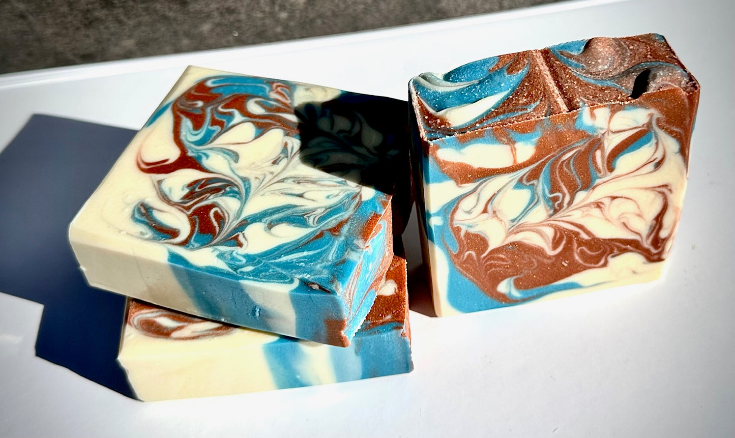 Three pieces of marbled soap with brown, blue, and white swirled pattern on a white surface.